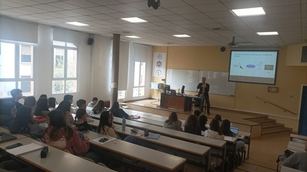 A lecture hall with a teacher in front of it. Students listening to a lecture.