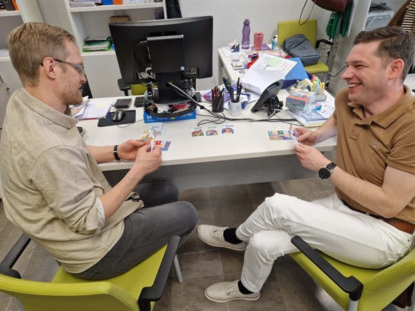 Two men sitting at a table holding playing cards